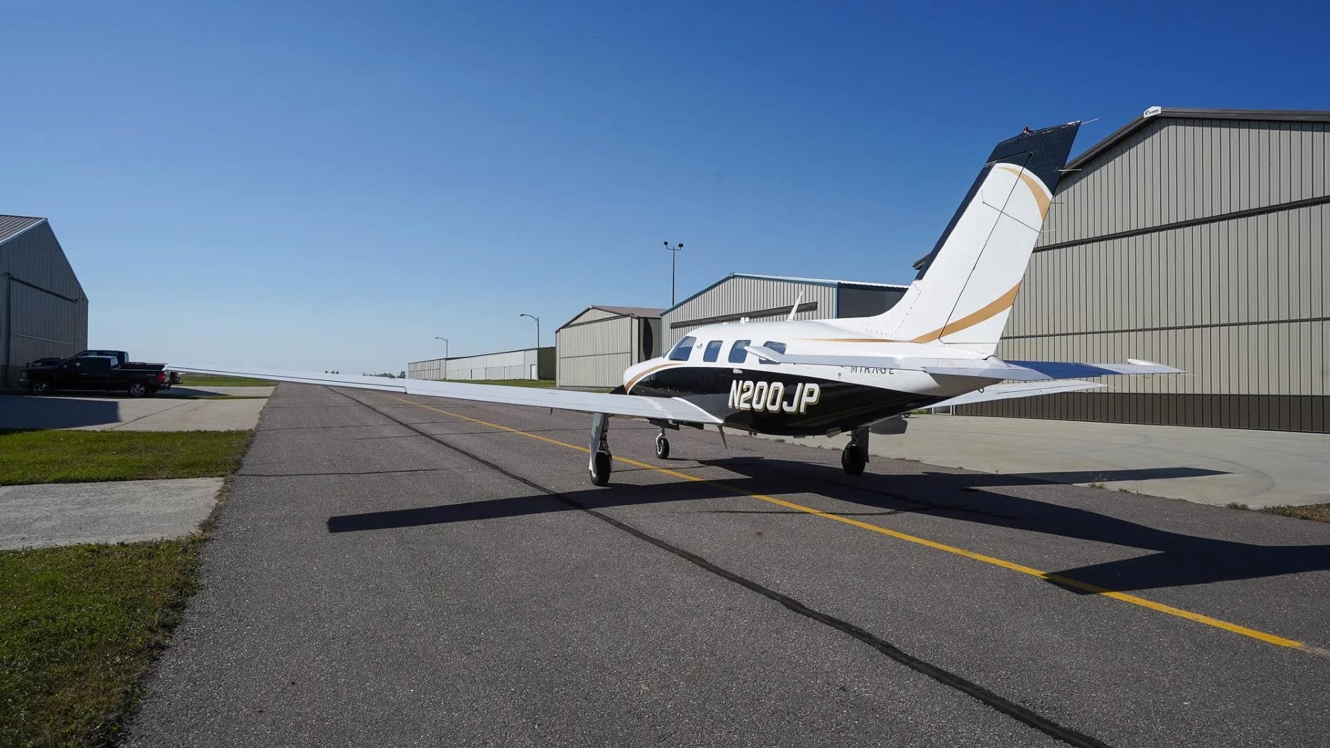 A rear-side view of a white and black Piper Mirage N200JP with gold accents on an airfield.