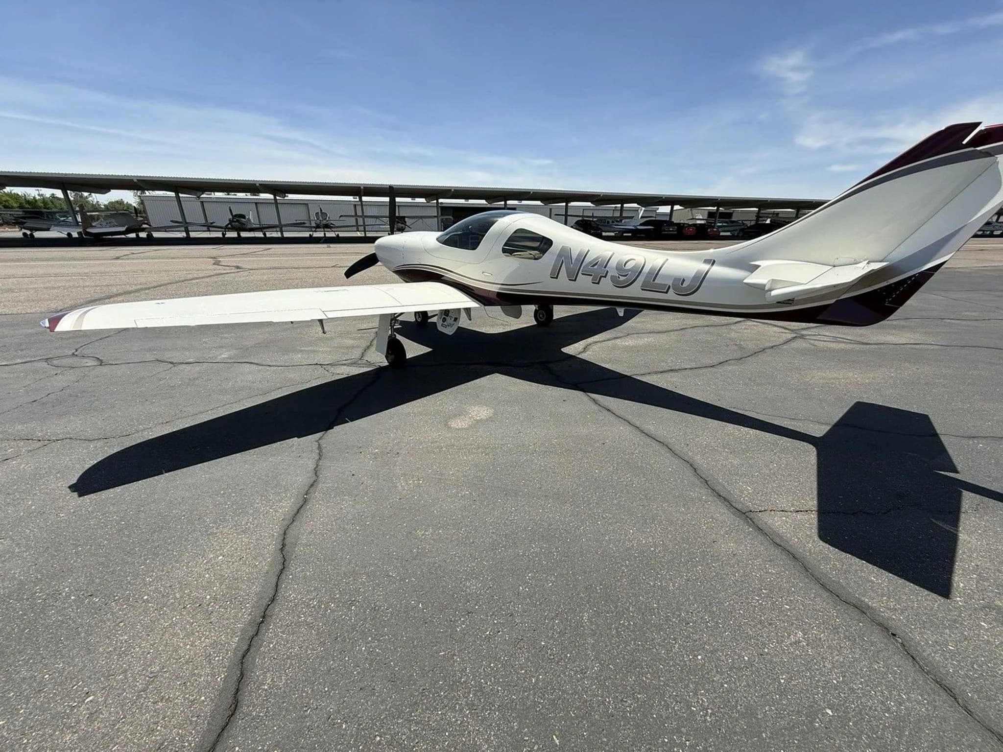 A rear-quarter view of the white and maroon single-engine aircraft (N49LJ) parked on an asphalt apron.