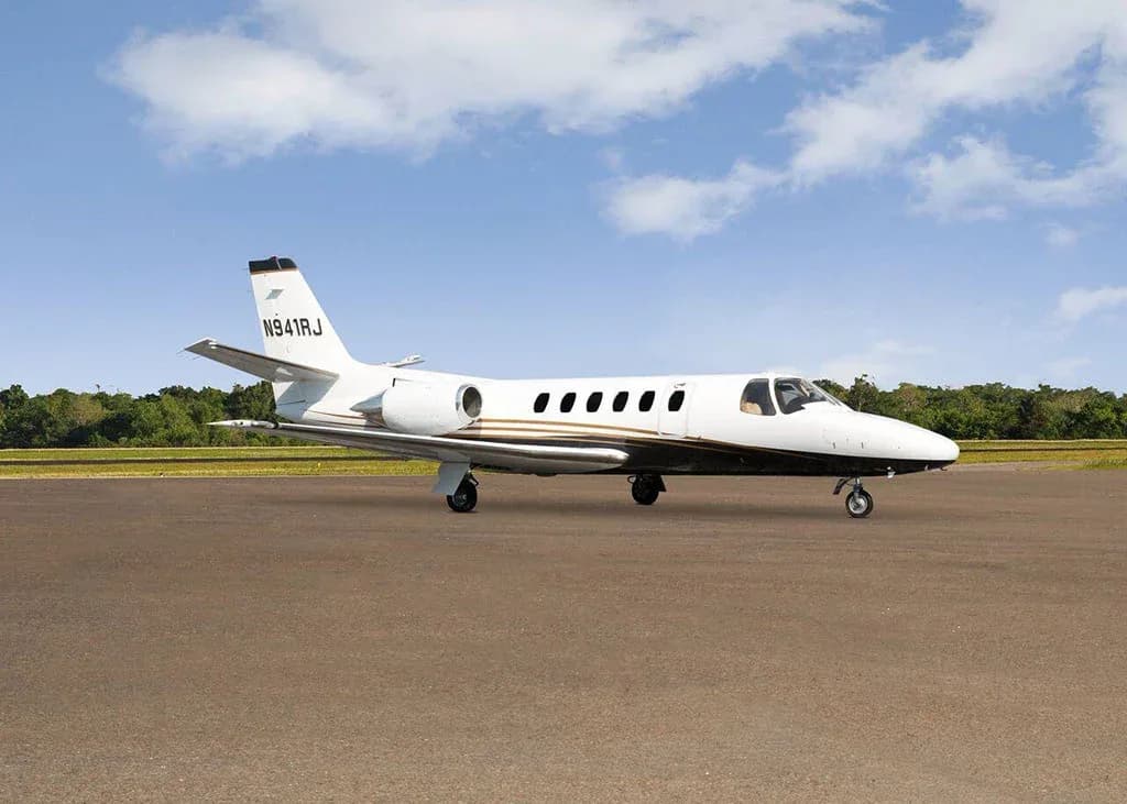 A white and black Cessna Citation business jet N941RJ with gold stripes is parked on a tarmac under a partly cloudy sky, viewed from the front-right.