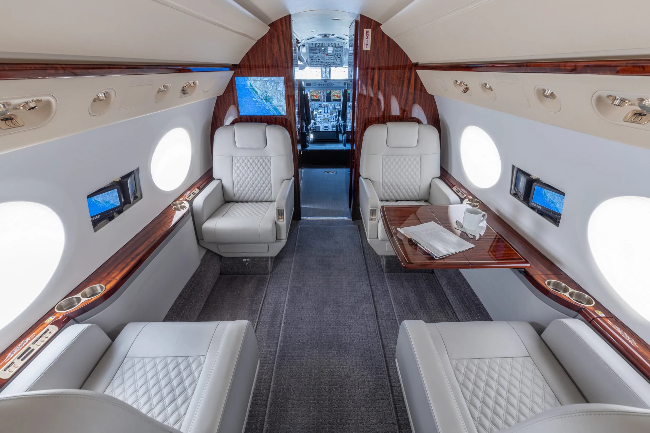 View of the aircraft interior with white leather seats and wood trim, looking towards the cockpit.