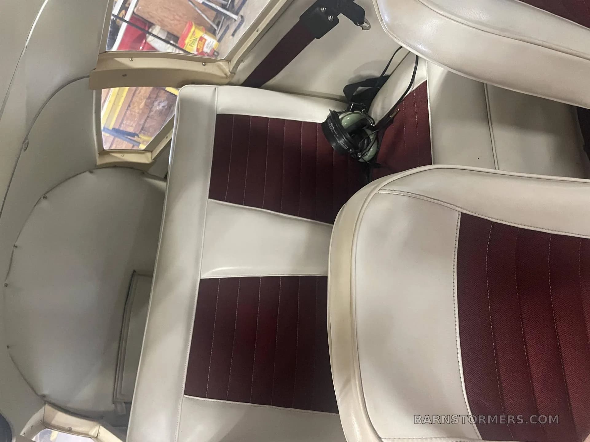 The interior cabin of a small aircraft, showing white and maroon upholstered seats.