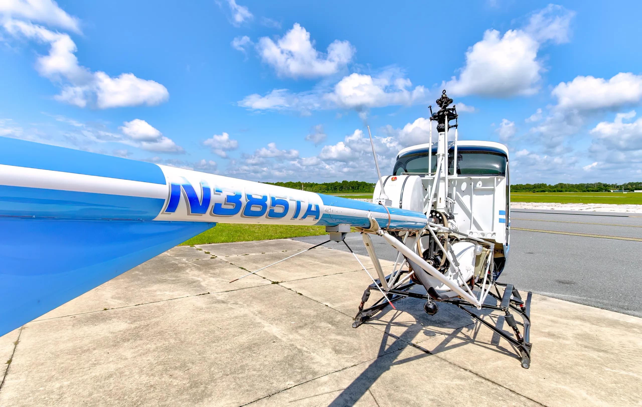 A close-up view of the blue and white tail boom of a Schweizer 300CBi helicopter, showing registration N385TA, on an airfield.