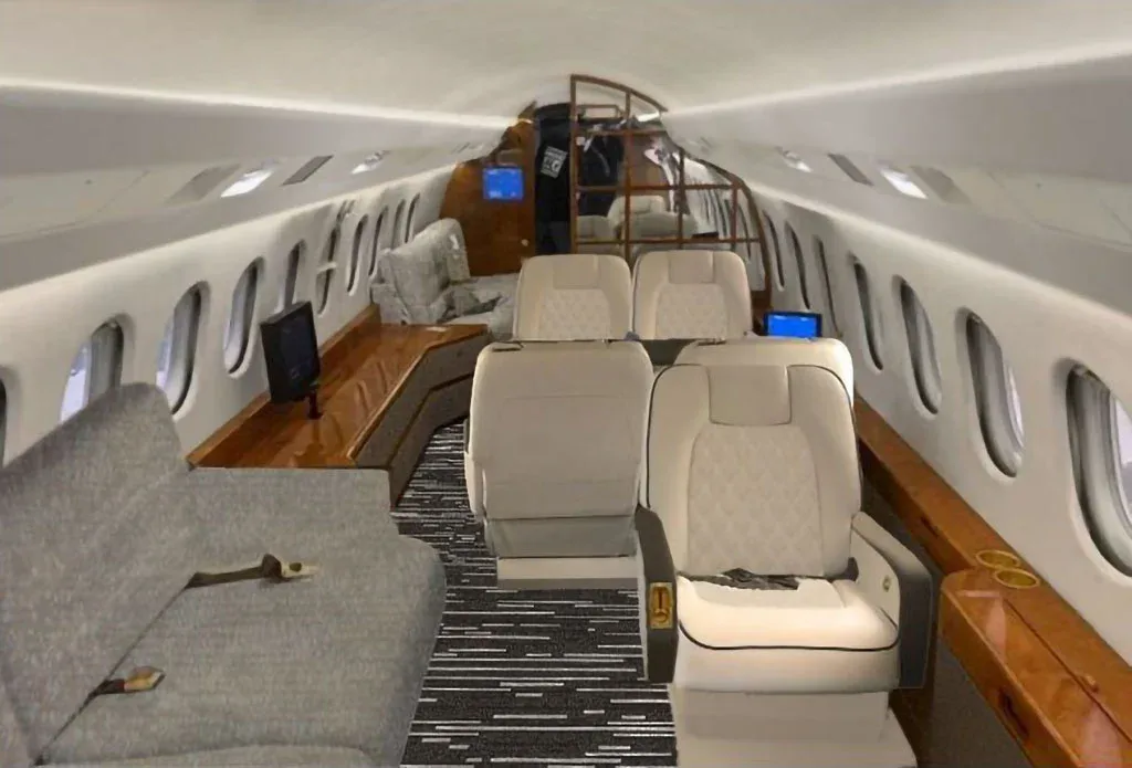A luxurious aircraft cabin features light-colored quilted seats, a grey sofa, and polished wood paneling.