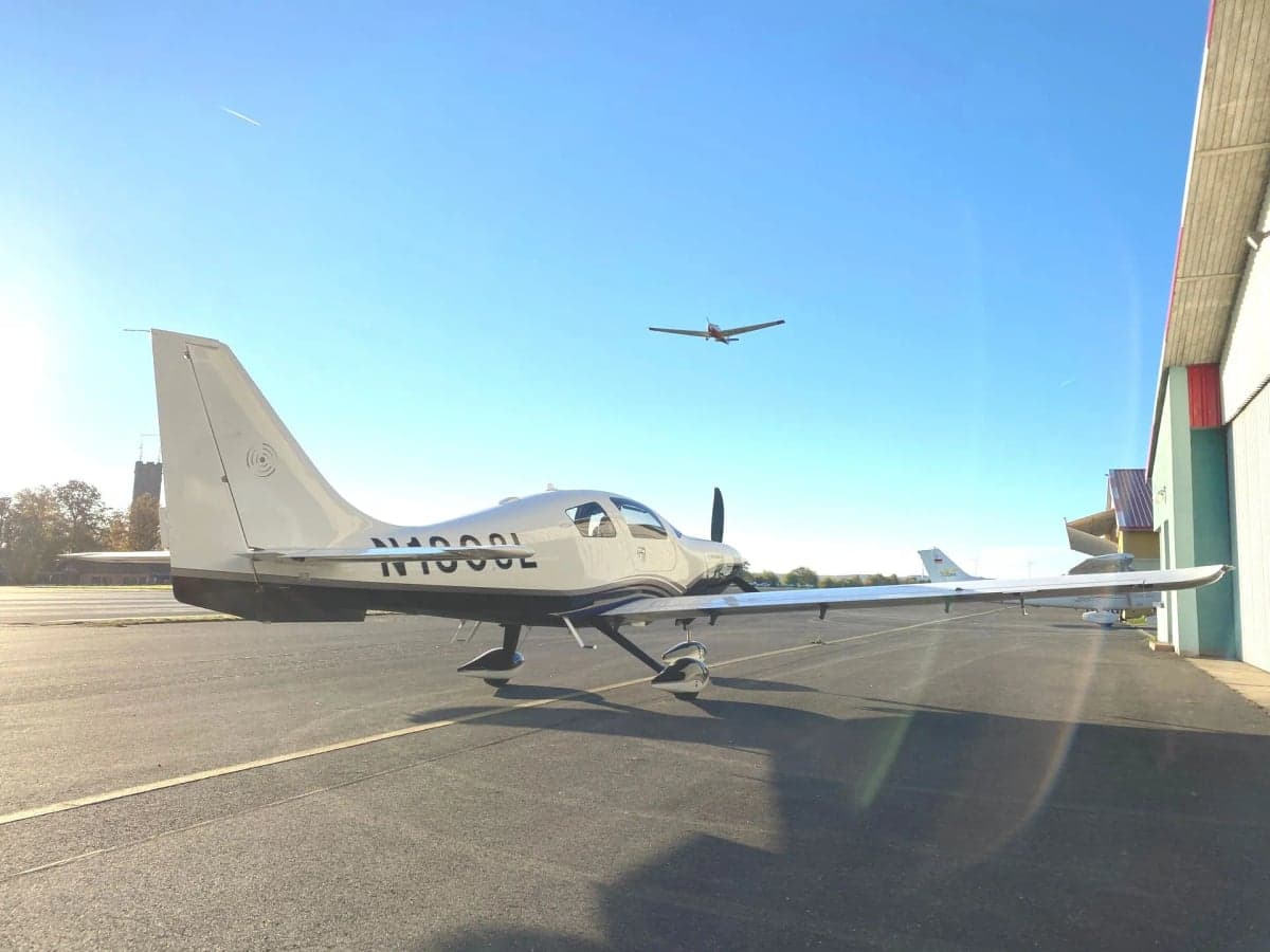 A rear view of the Cirrus Columbia 400 parked on the tarmac in front of a hangar.