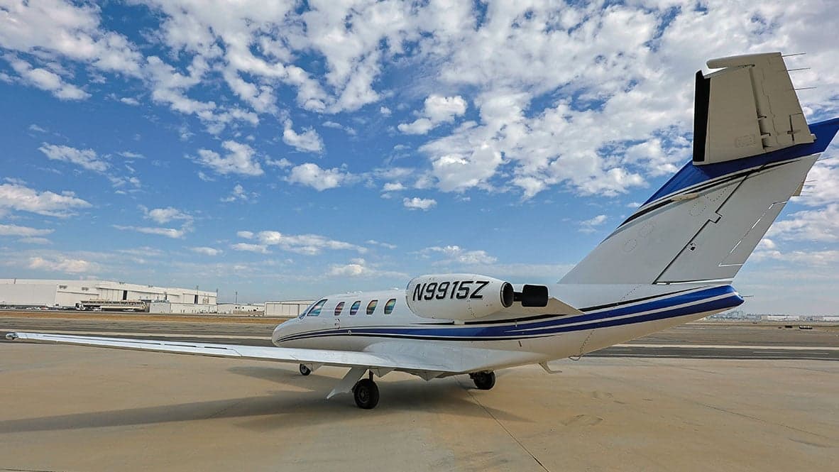 A white and blue Cessna Citation CJ1 aircraft with registration N9915Z parked on the tarmac with a cloudy sky overhead.