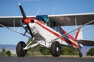 A Piper Super Cub aircraft with a red and white paint scheme is parked on the tarmac.