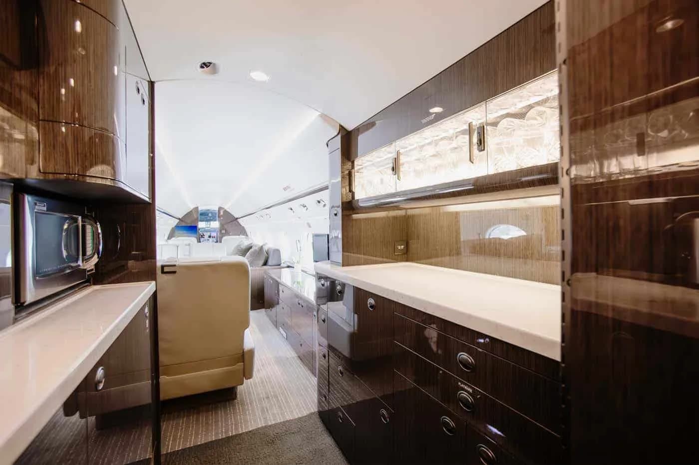 A modern aircraft galley with dark wood cabinetry, white countertops, and a microwave oven.