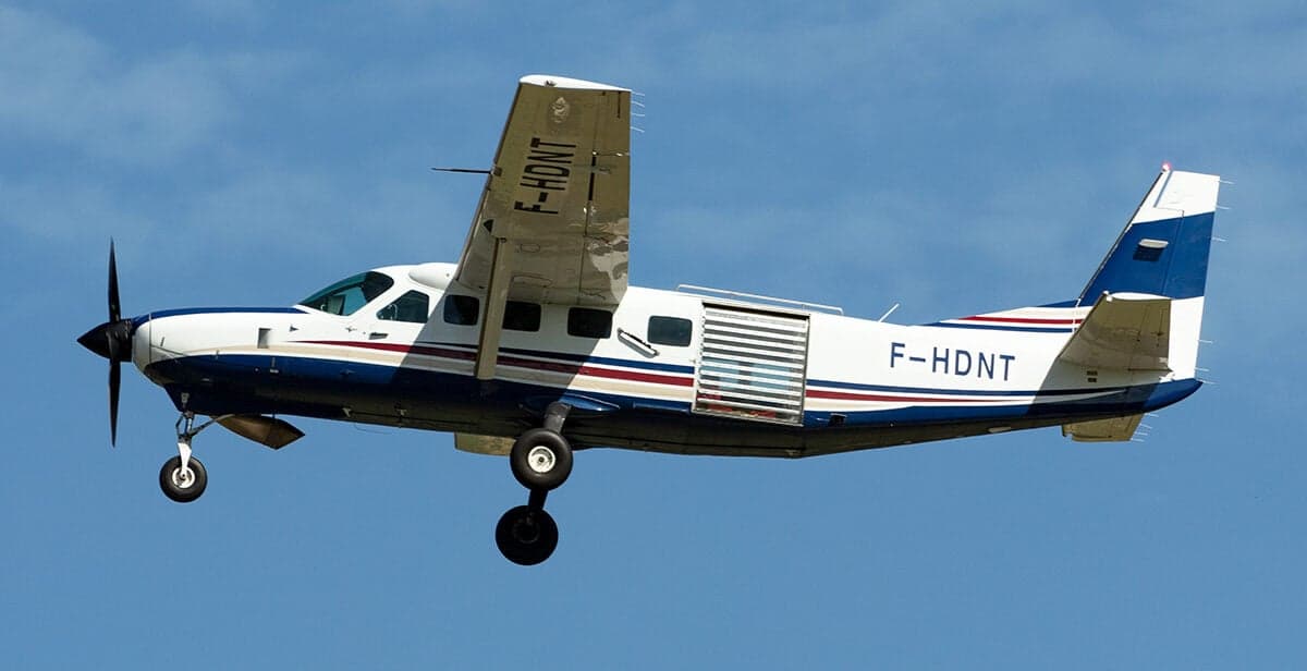 Side view of a white and blue painted Cessna 208 Caravan in flight.