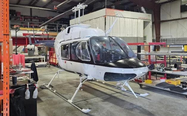 A white and black Bell 206 helicopter parked inside a hangar, viewed from the front-right.