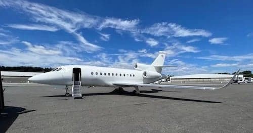 Exterior view of a white Falcon jet parked on the tarmac with the door open.