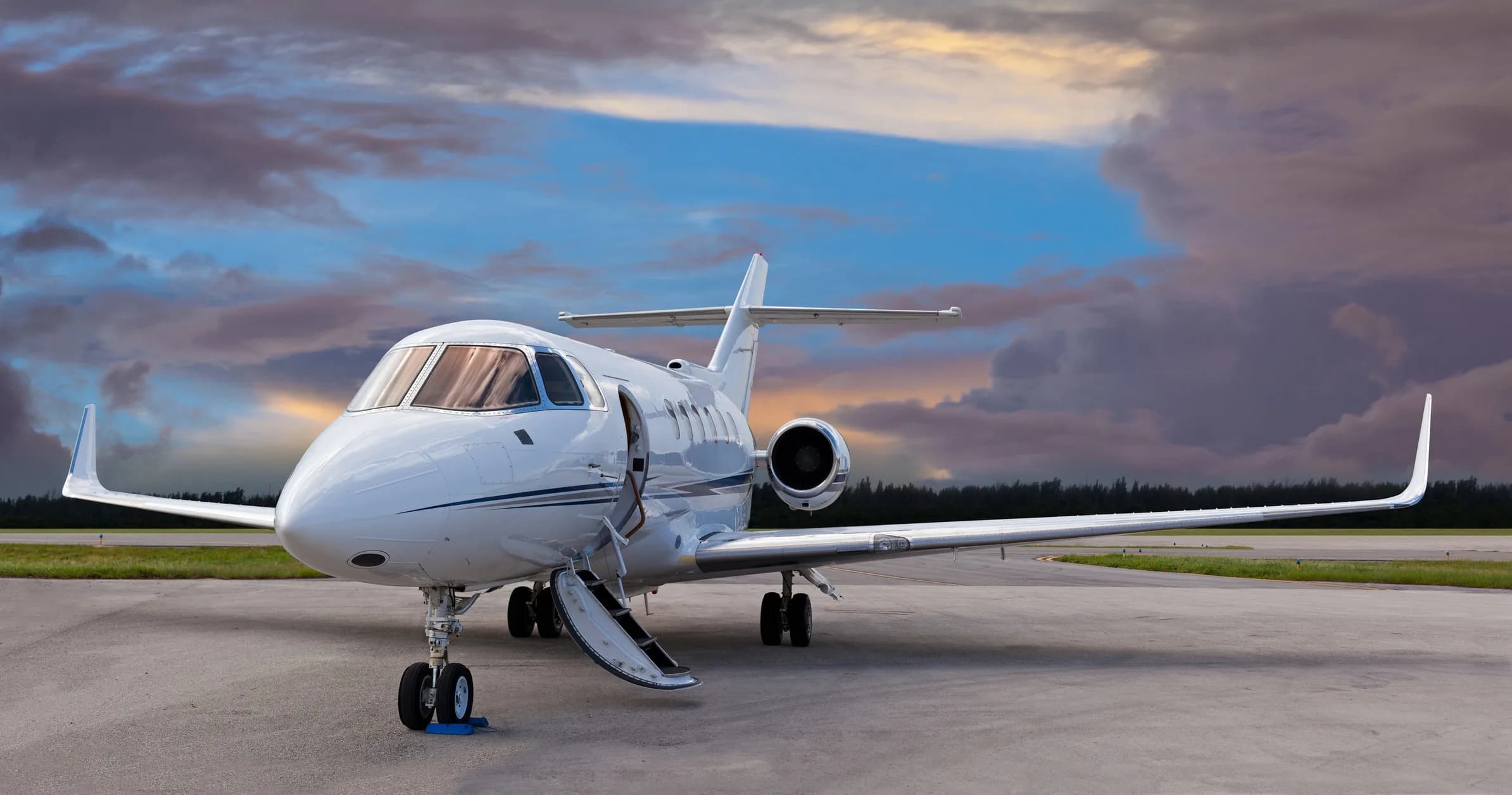 White jet with open door parked on the tarmac at sunset.