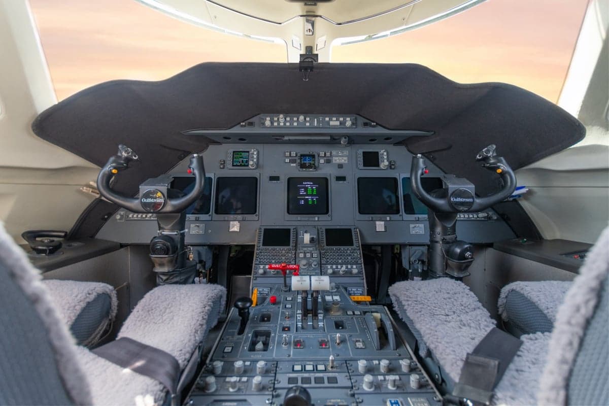 The cockpit of a business jet with multiple digital displays, control yokes, and a central throttle quadrant.