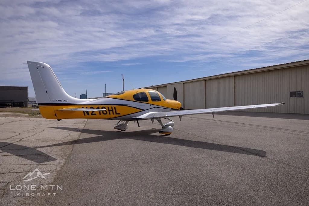 A Cirrus SR22 aircraft with yellow and silver paint scheme parked on an airfield, showing the rear left.