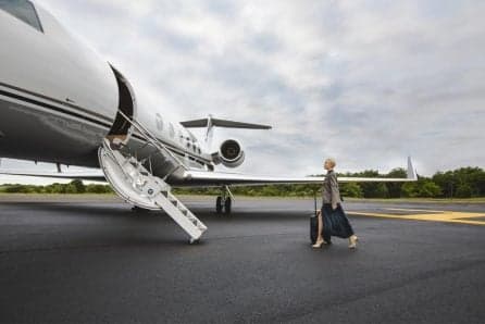 A woman walks toward the open door of a private jet with a suitcase.