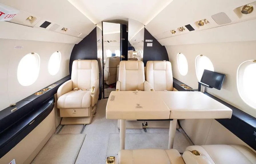 The luxurious interior cabin of a business jet, featuring beige leather seats and a large fold-out table.