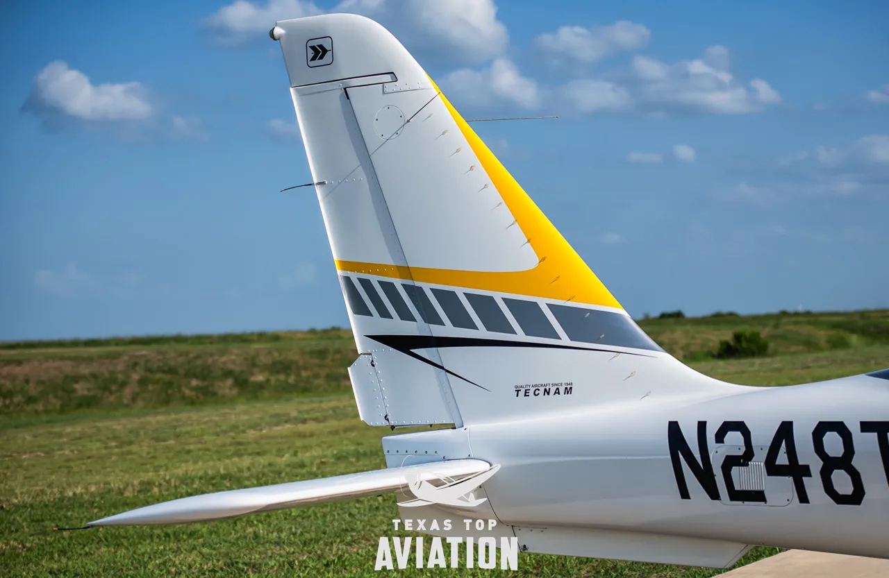 A close-up of the white and yellow tail of a Tecnam aircraft, showing the 'Tecnam' logo and part of the registration.