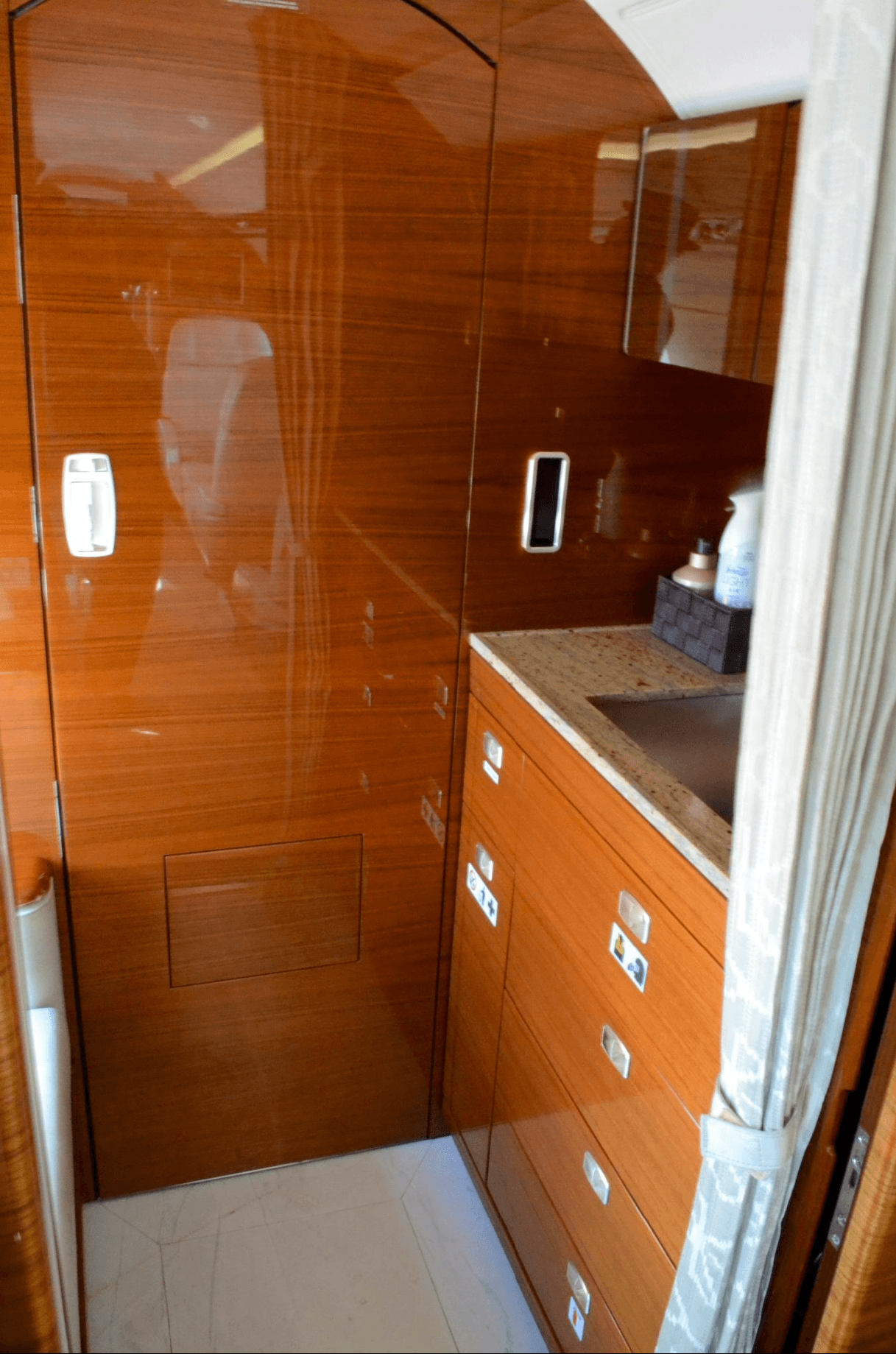 A luxurious aircraft galley or lavatory area featuring polished wood paneling, a granite countertop with a sink, and a privacy curtain.