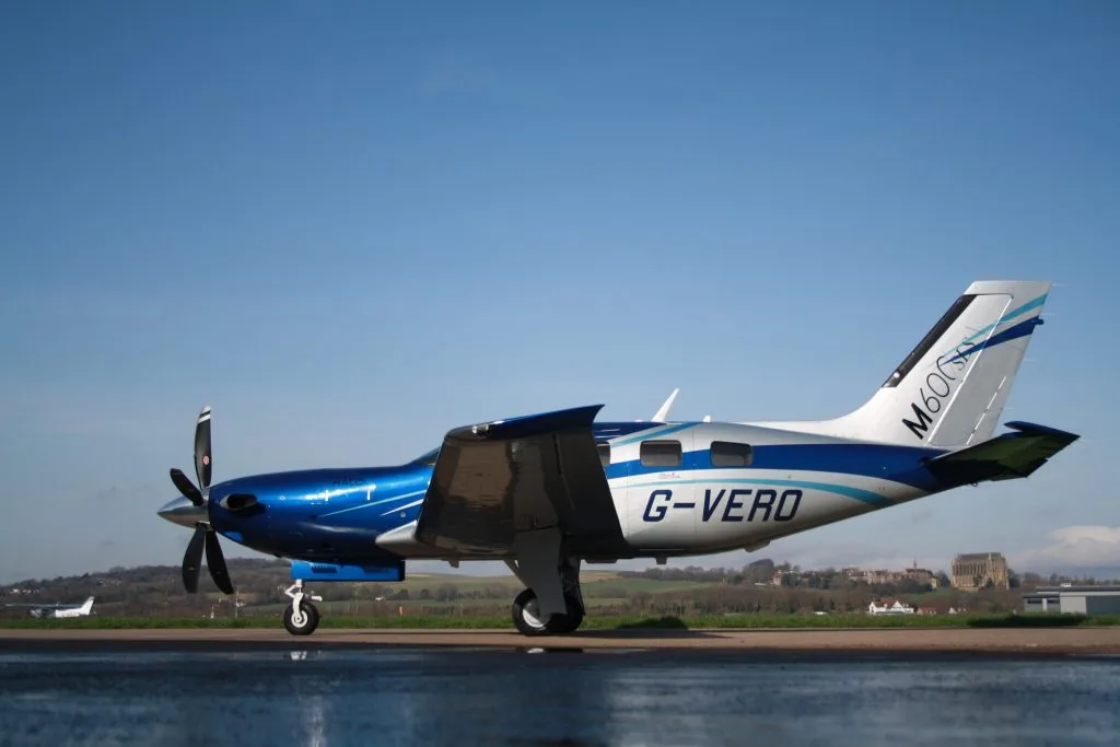A side view of a blue and silver Piper M600SLS aircraft (G-VERO) with its flaps extended, parked on an airfield.