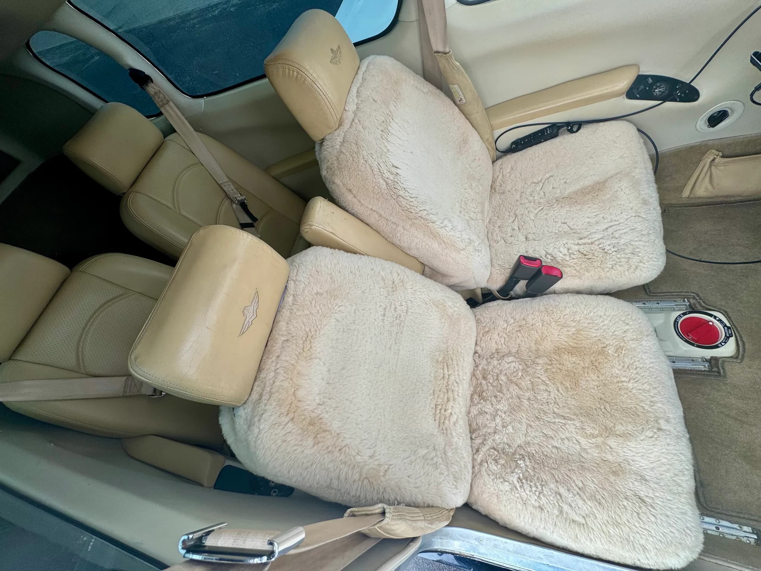 The interior cabin of a Mooney aircraft, showing beige seats, some covered with white sheepskin, and a skylight.