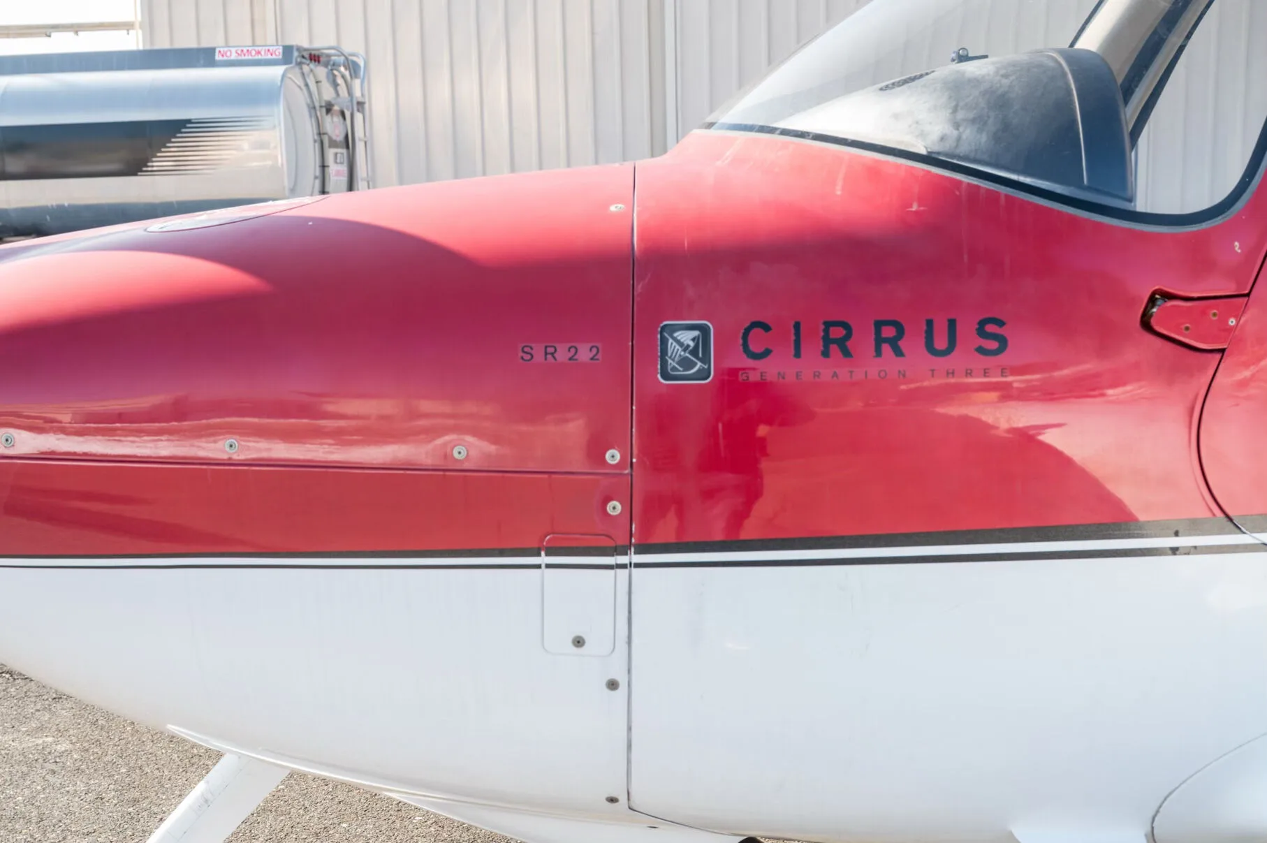 A close-up of the red and white fuselage of a Cirrus SR22 aircraft, showing the 'SR22' and 'CIRRUS' logos.