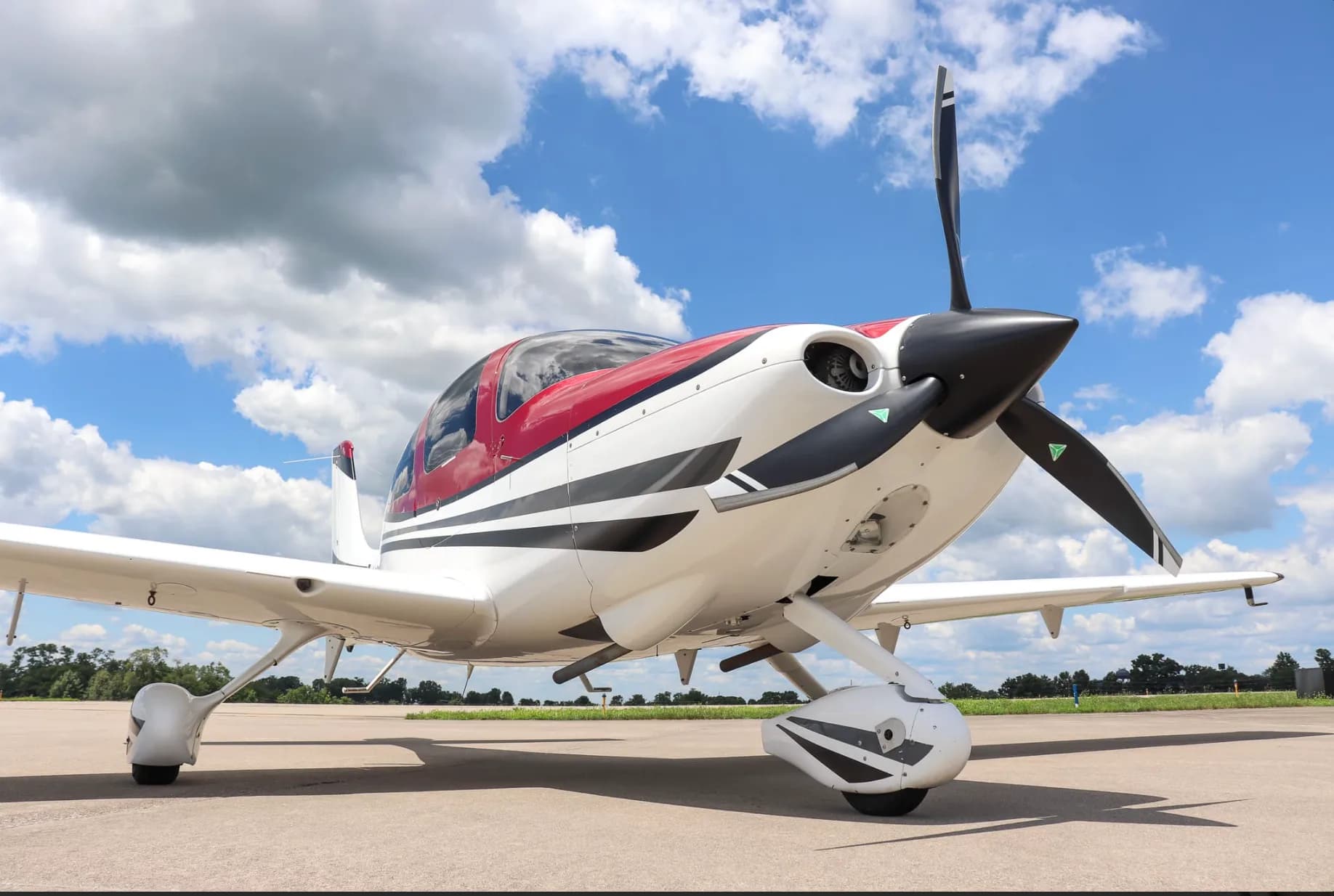 A low-angle three-quarter front view of a white and red single-engine aircraft with its doors closed on an airfield.