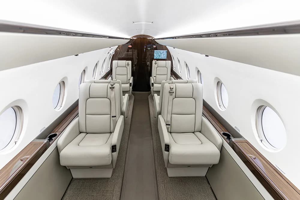 A wide-angle view of a luxurious aircraft cabin with light-colored leather seats arranged in a club configuration.
