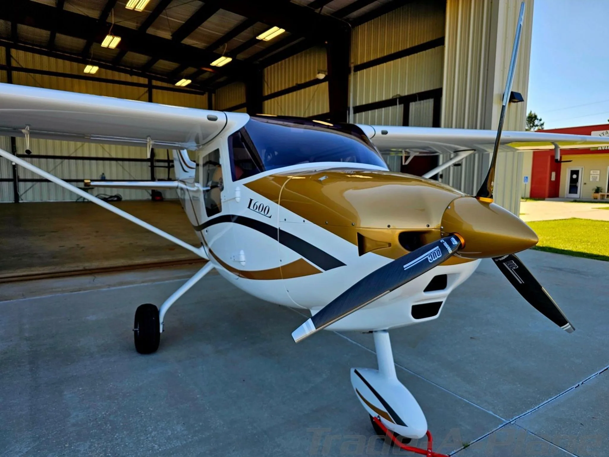 A front-right view of the white and gold I600 aircraft (N152RT) with its propeller, parked outside a hangar.