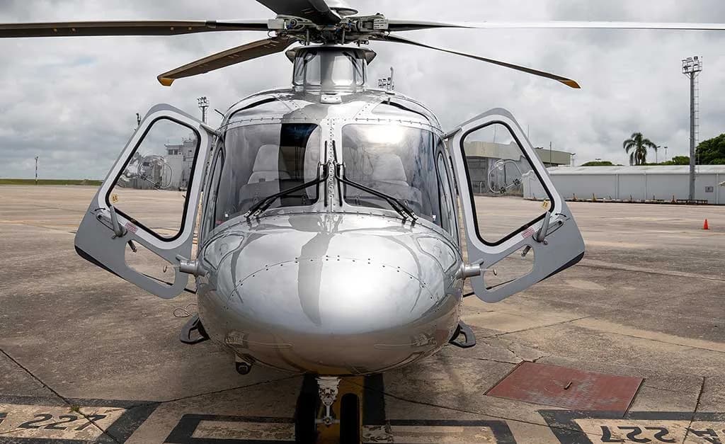 Front view of the silver AgustaWestland AW169 helicopter with both cockpit doors open, parked on an airfield.