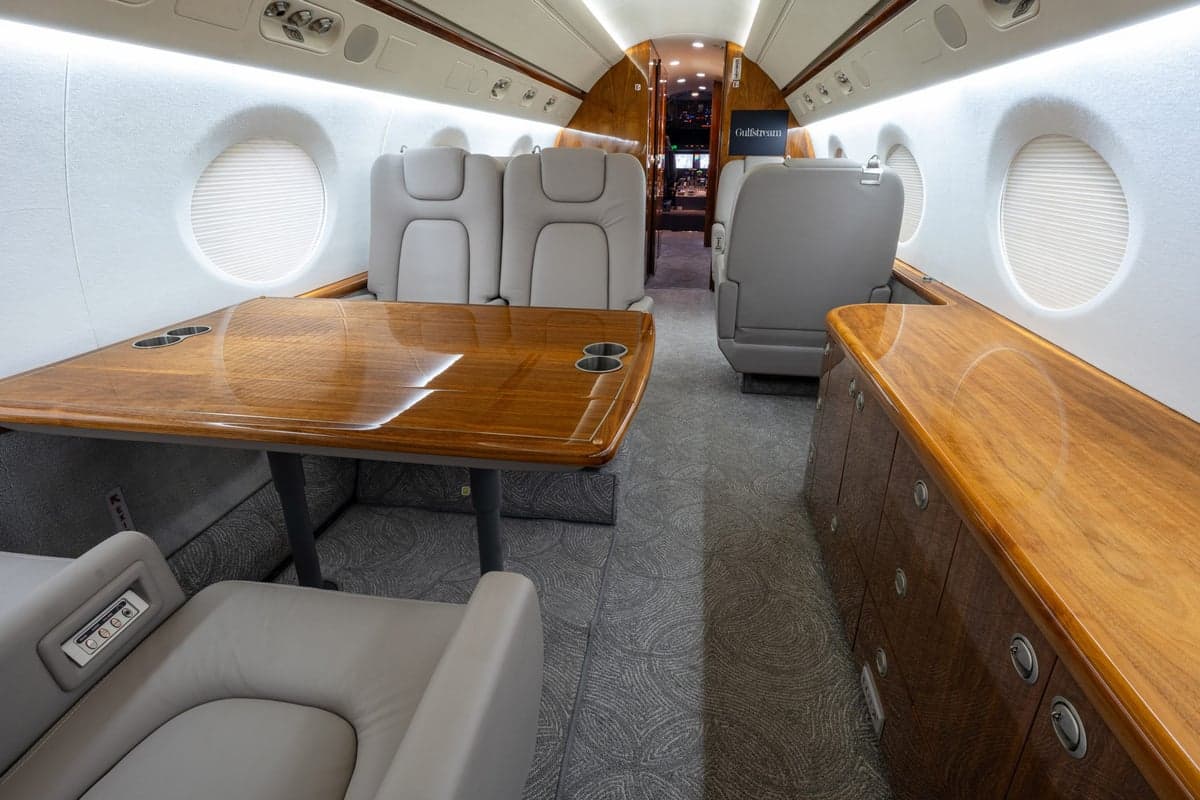 The aircraft's interior features a table, seating, and wood trim.