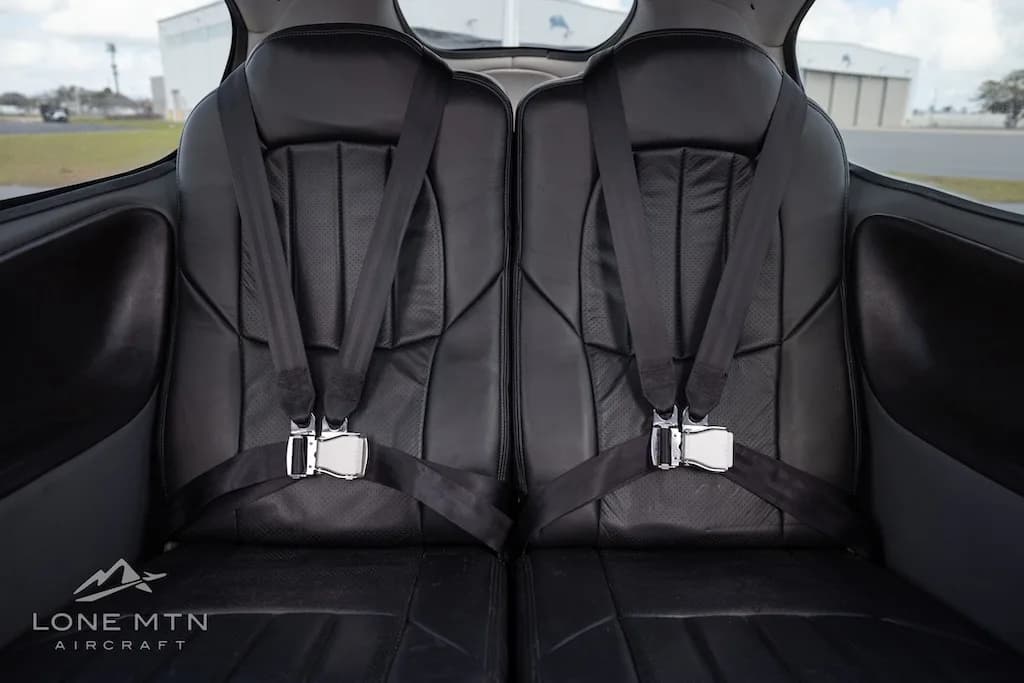A straight-on view of the black leather rear passenger seats with seatbelts inside the aircraft cabin.