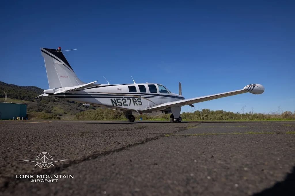A low-angle side view of a white Beechcraft Baron N527RS with black and gold stripes parked on an asphalt runway.
