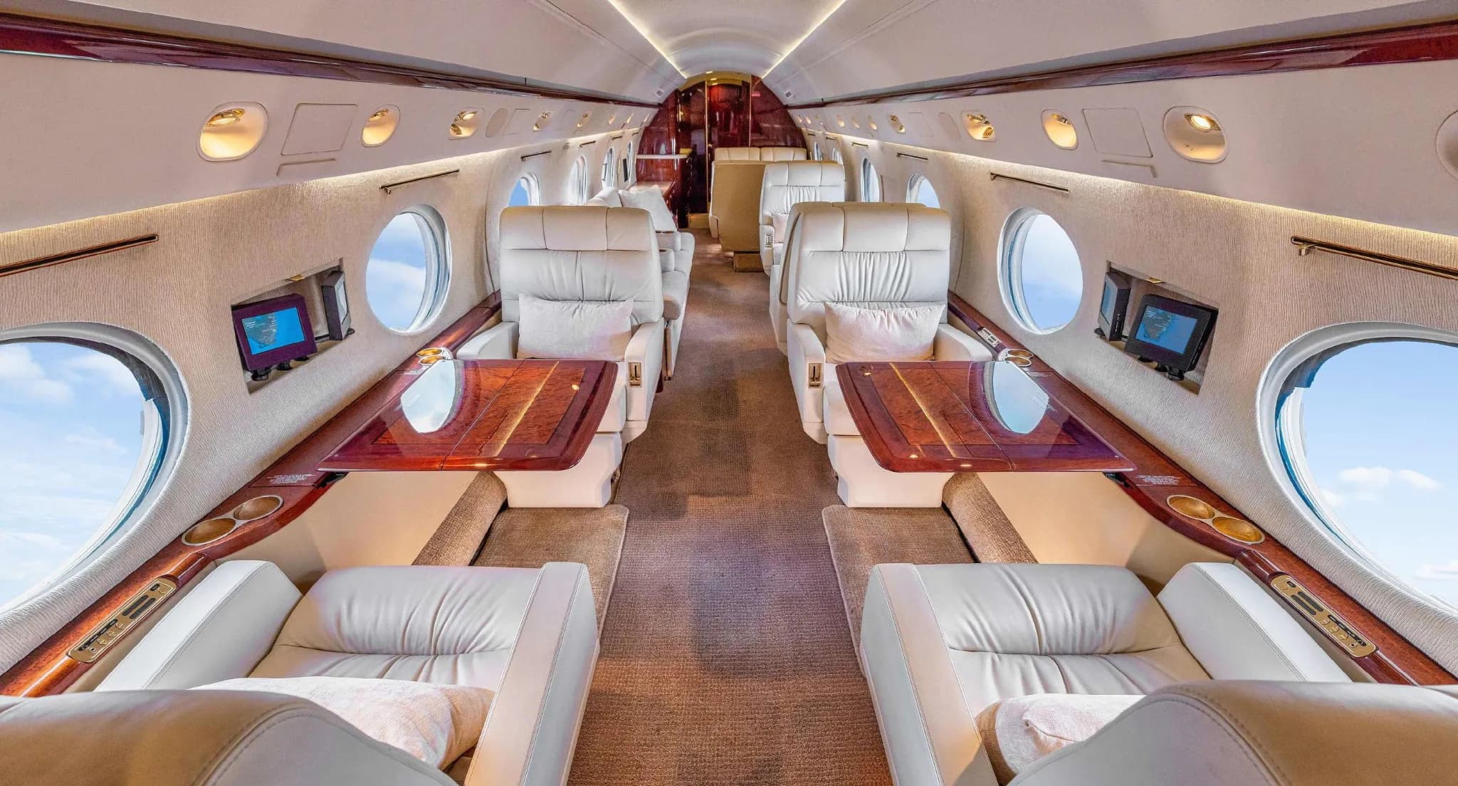 The elegant cabin interior of a Gulfstream G550, showing cream leather seats with fold-out tables.