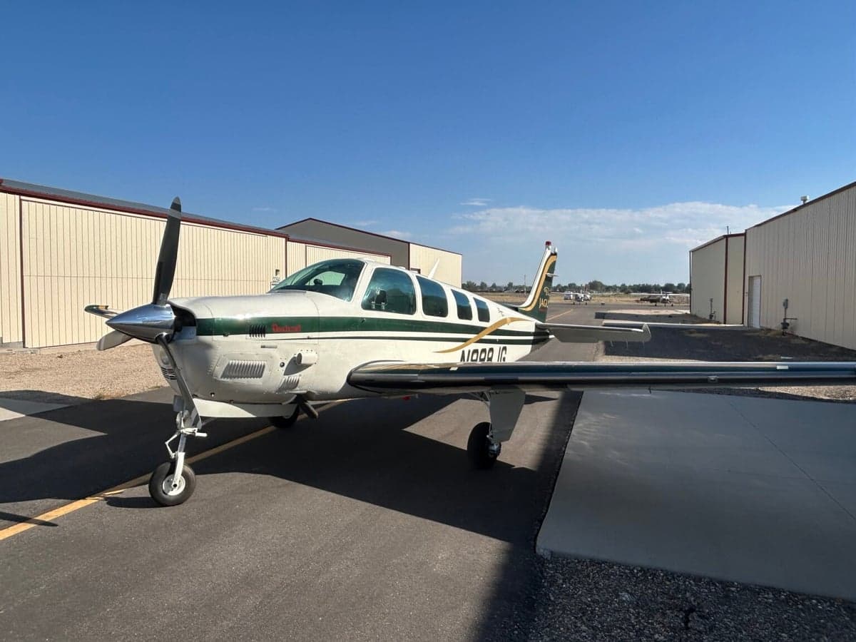 A Beechcraft Bonanza N988JG parked on the tarmac in front of a hangar on a sunny day.