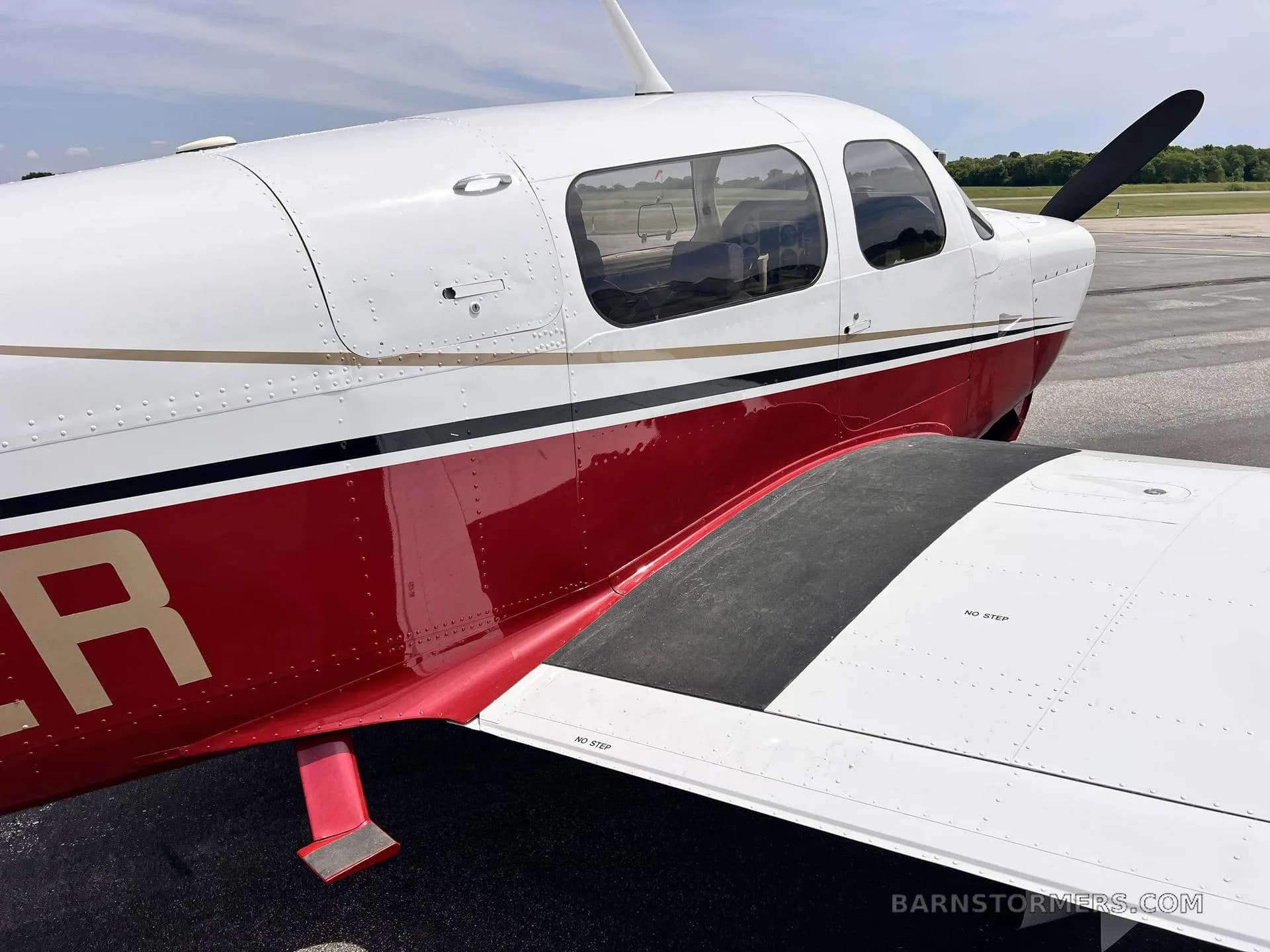 A close-up view of the white and red fuselage and wing of a single-engine propeller aircraft.