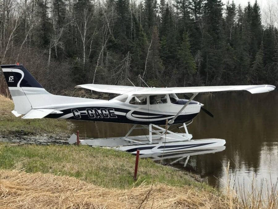 A Cessna floatplane is parked on the shore of a lake.