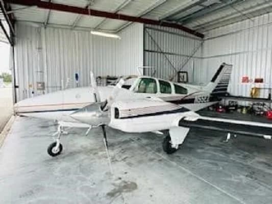 A white and blue twin-engine aircraft, N55EZ, is parked inside a hangar, viewed from the front-left.