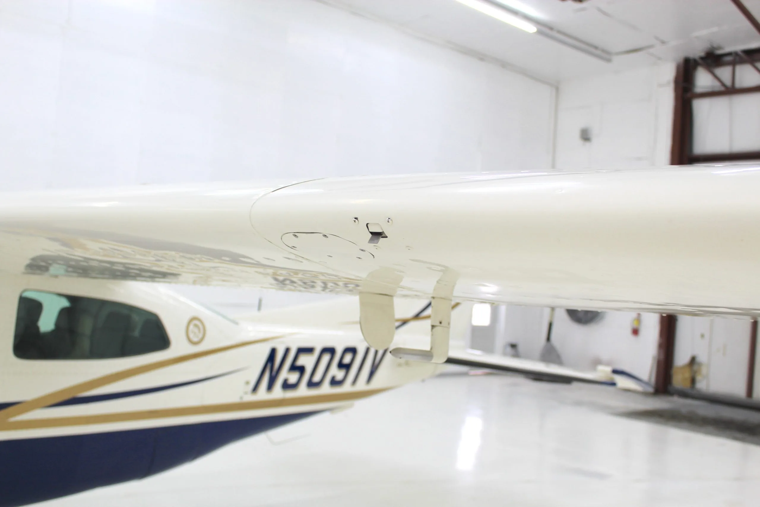 Underside view of the wing and fuselage of the Cessna 206 aircraft, N5091V, in a hangar.