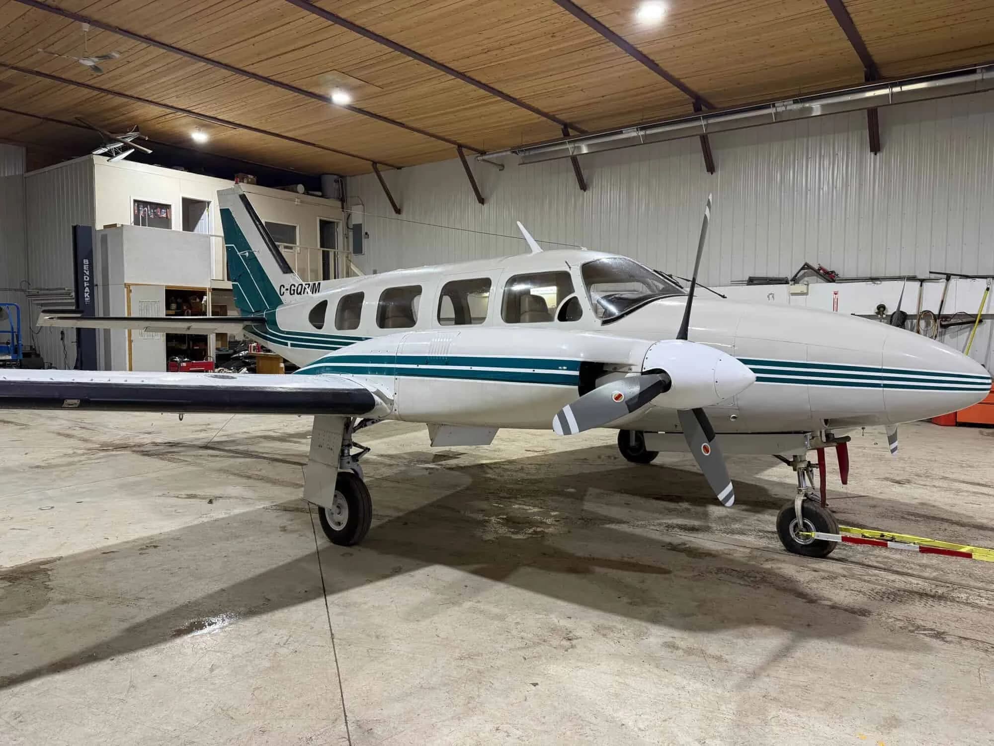 A white and green twin-engine aircraft, registration C-GQRM, parked in a hangar.