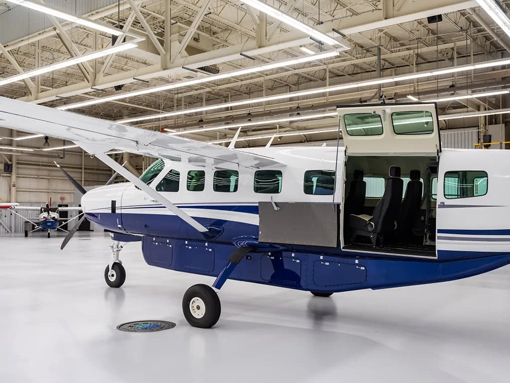A side view of the white and blue Cessna Caravan with its large cargo door open in a hangar.