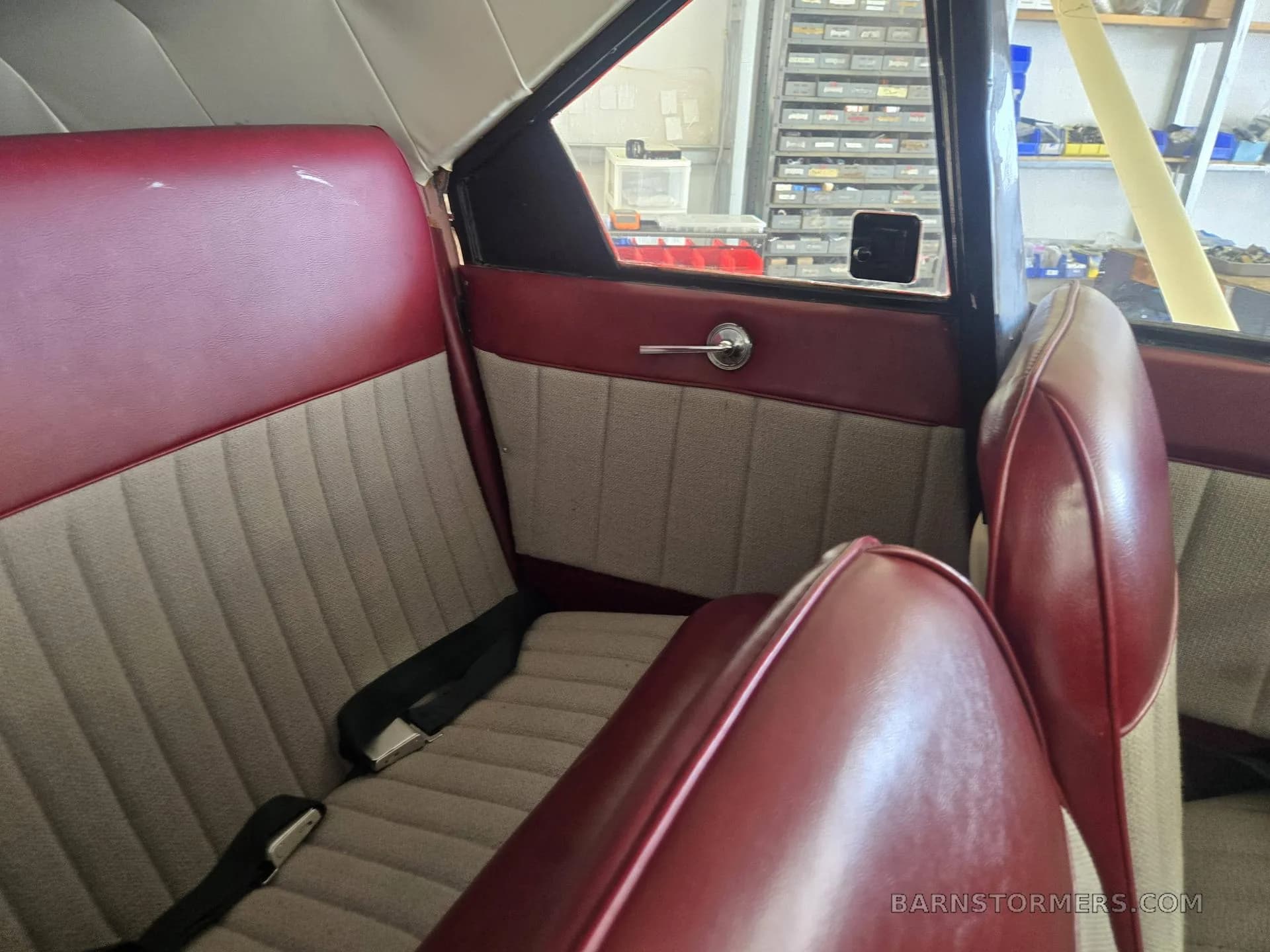 The interior cabin of a small aircraft, featuring red and beige upholstered seats with seatbelts.