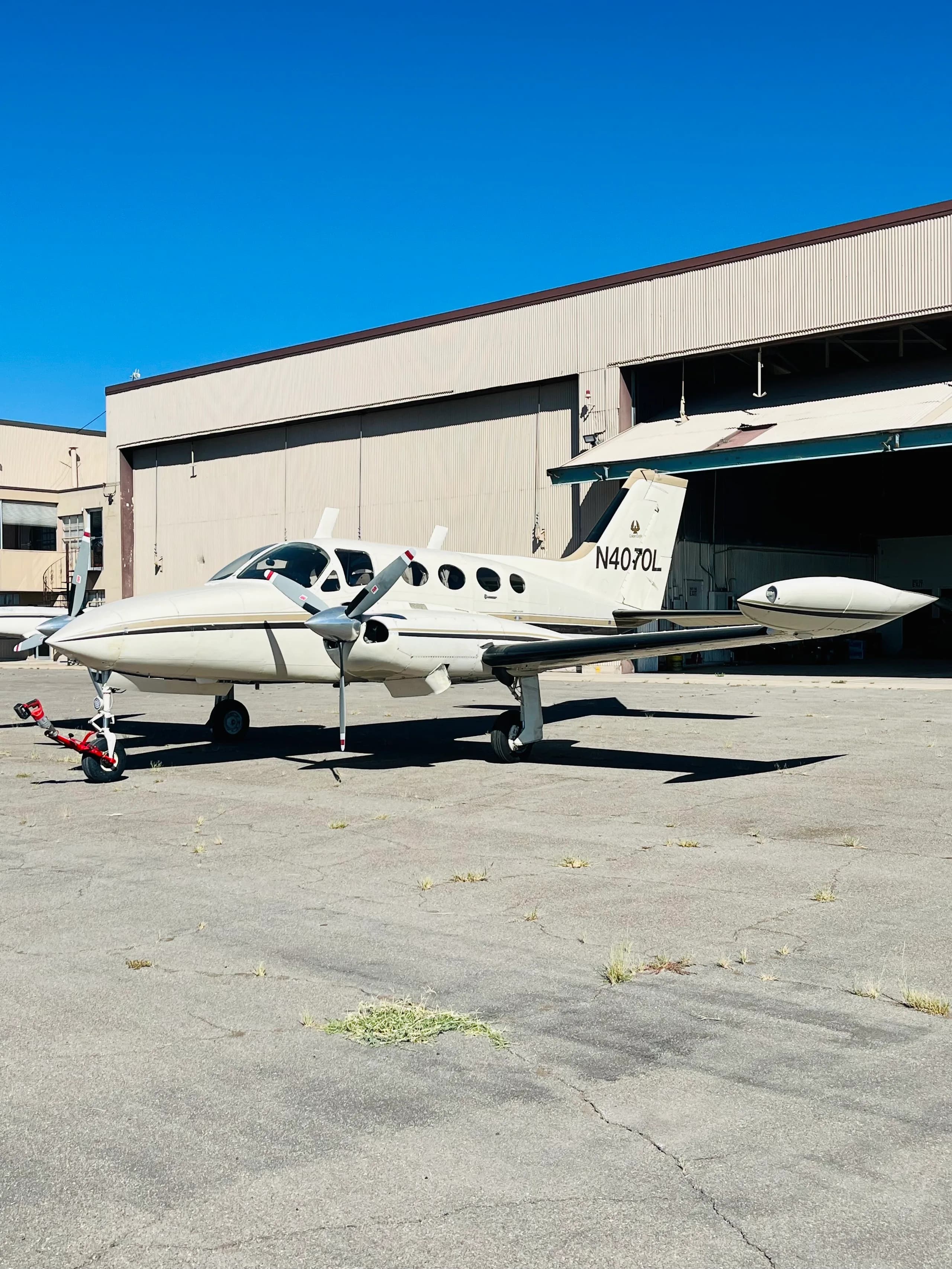 A white and gold Cessna 421 Golden Eagle (N4070L) parked on an airfield with hangars in the background.