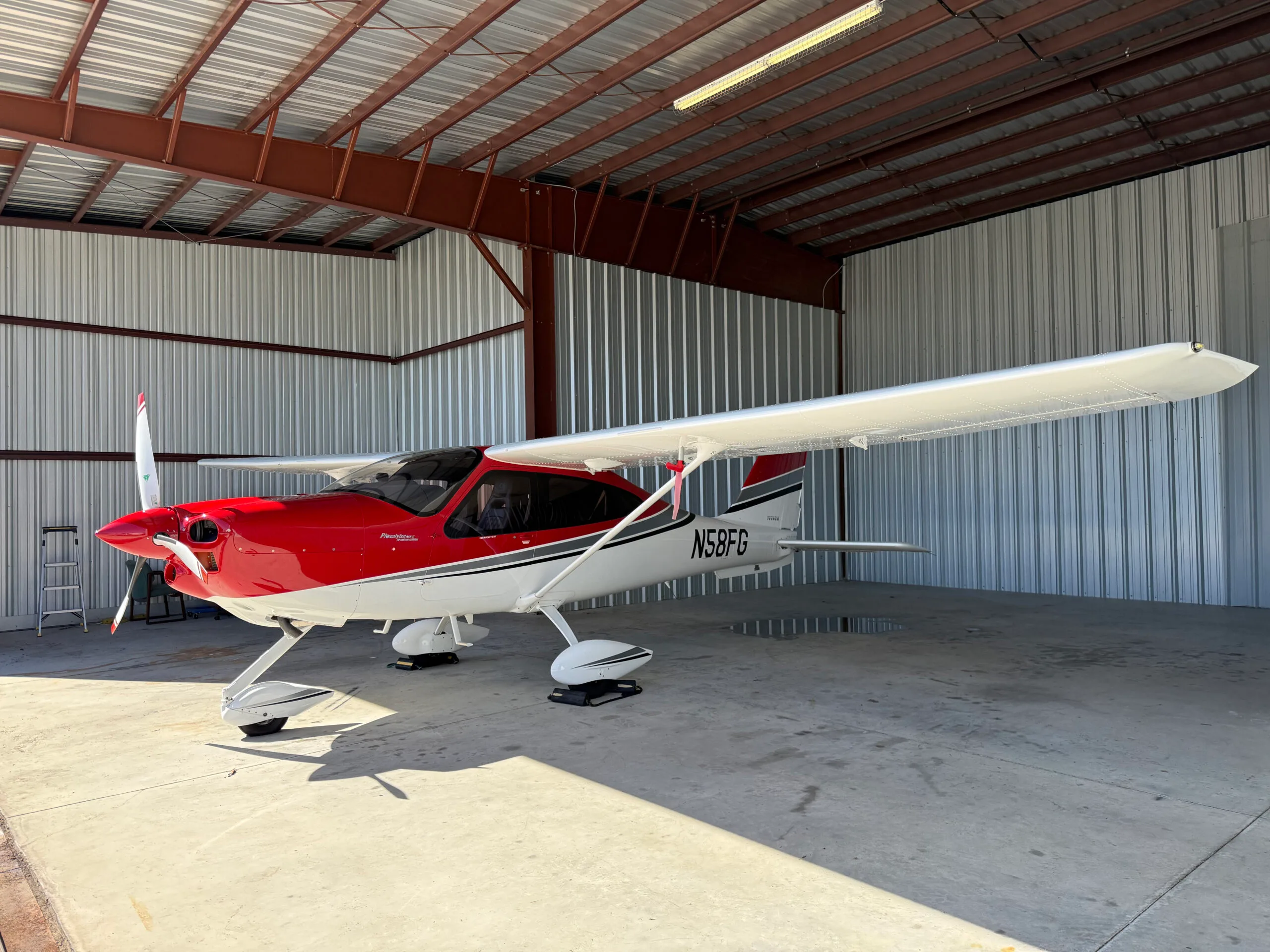 Tecnam P2010 aircraft N58FG parked in a hangar with a red and white paint scheme.