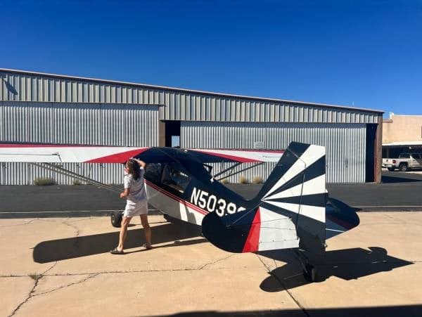 A black and white Maule aircraft with red stripes and a distinctive tail pattern, registration N5039G, parked on an airfield with a person standing nearby.