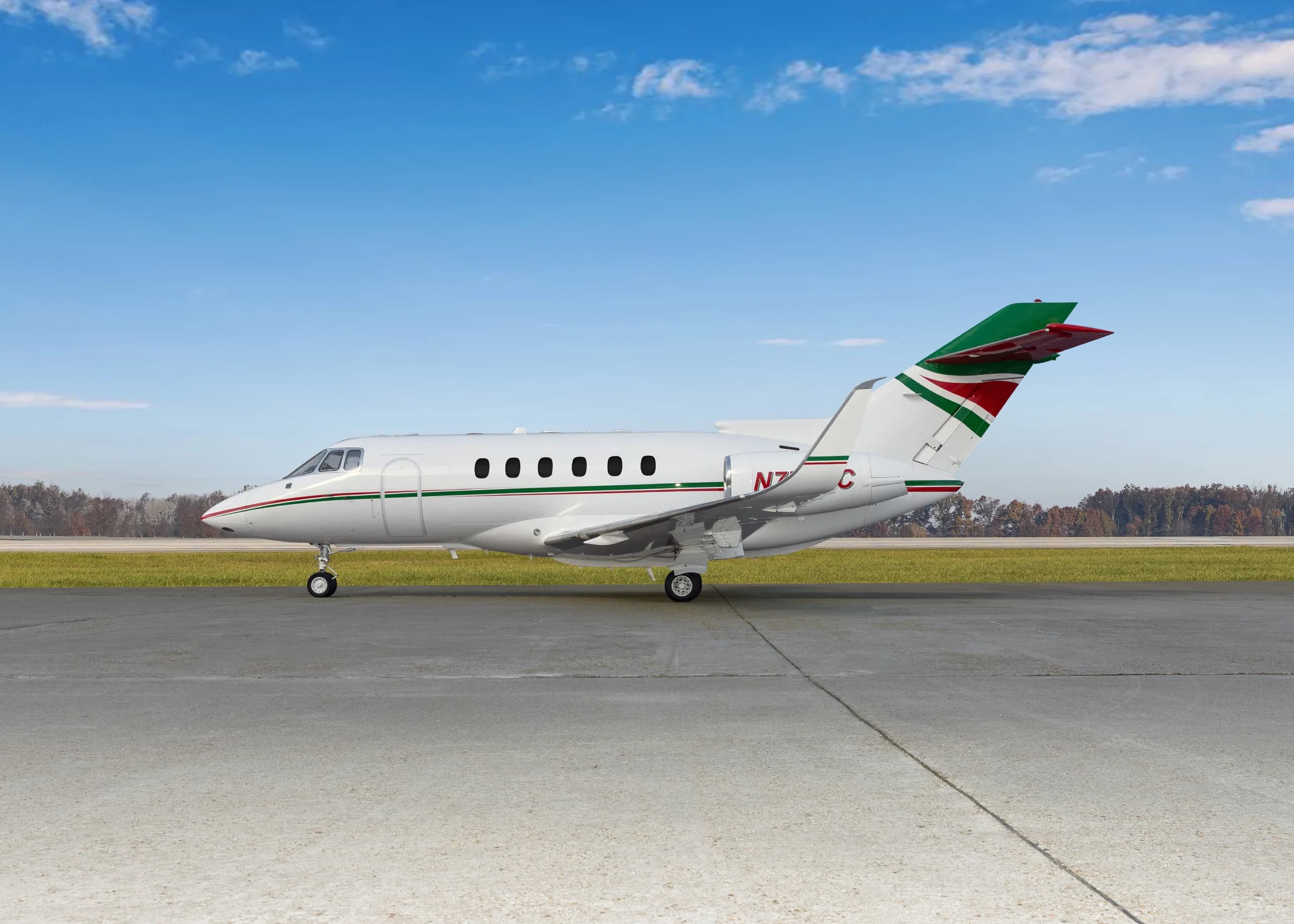 A white business jet with green and red stripes on the fuselage and tail, seen from the side on an airfield.