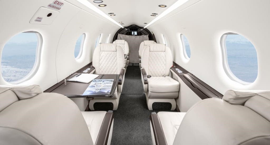Interior view of the aircraft cabin with white leather seats and a table.