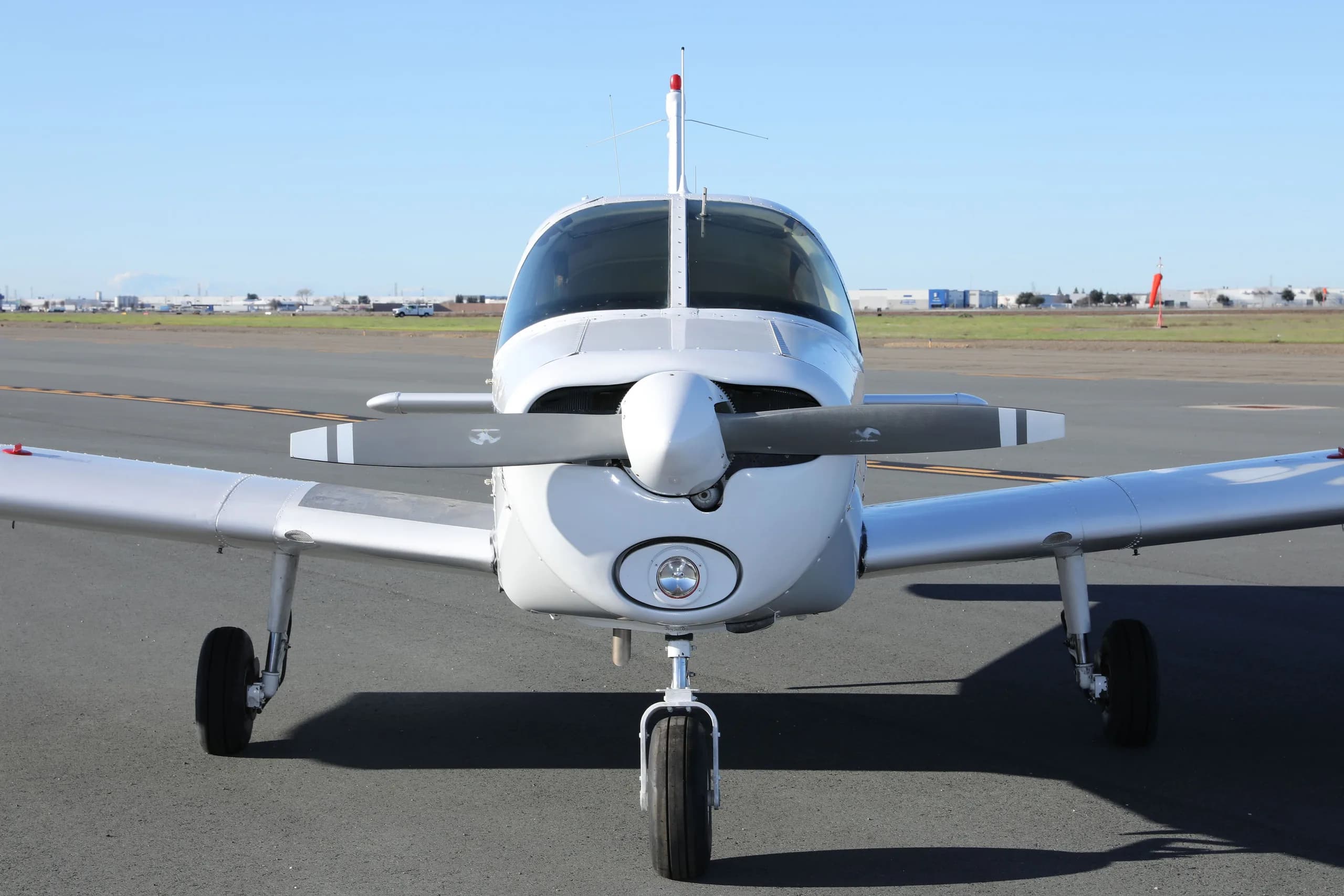 A head-on view of the white Piper Cherokee N38477 with its three-bladed propeller on an airfield.