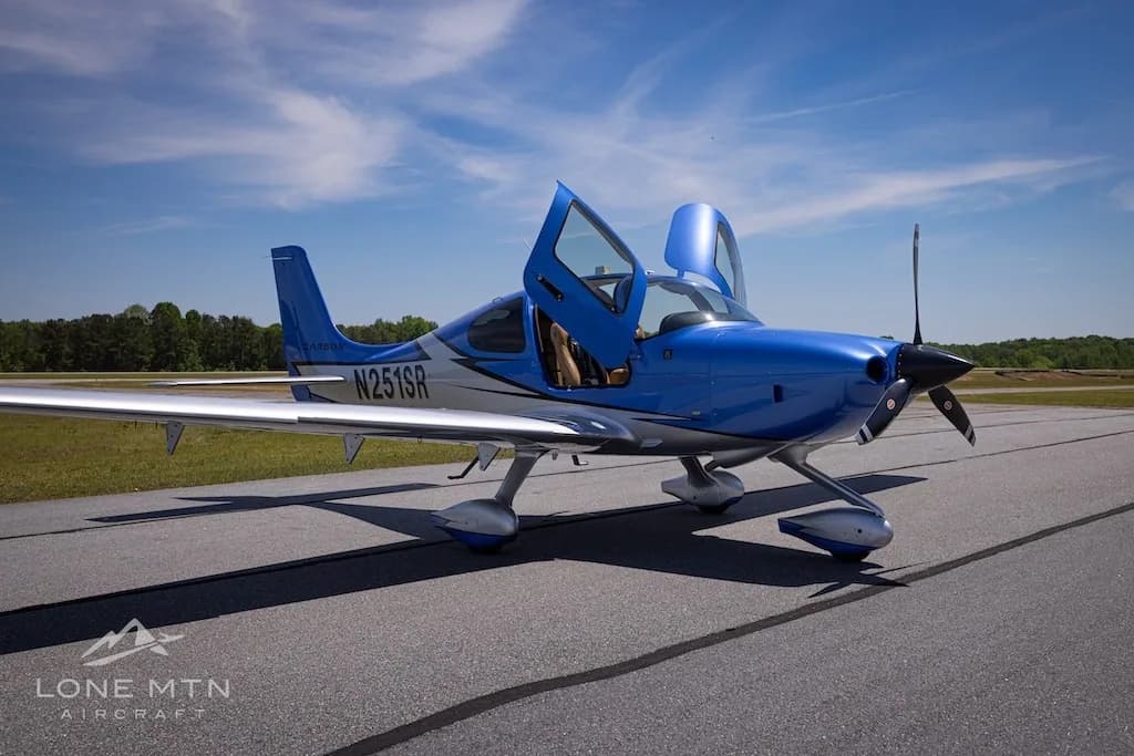 A front-side view of the blue and silver Cirrus SR20 aircraft (N251SR) with open doors on an airfield.
