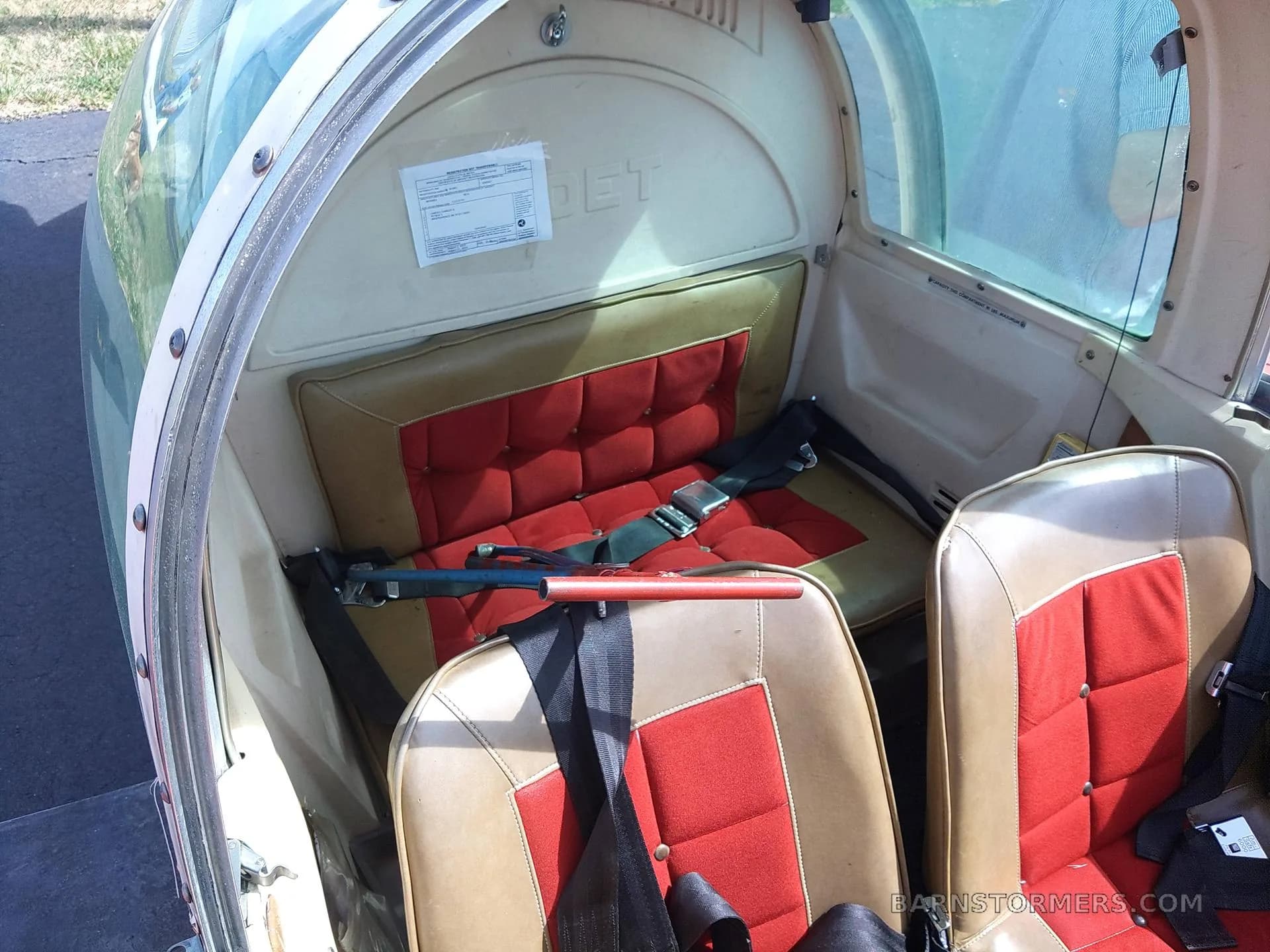 The aircraft's interior shows two-tone red and tan seats with seatbelts and a clear canopy.