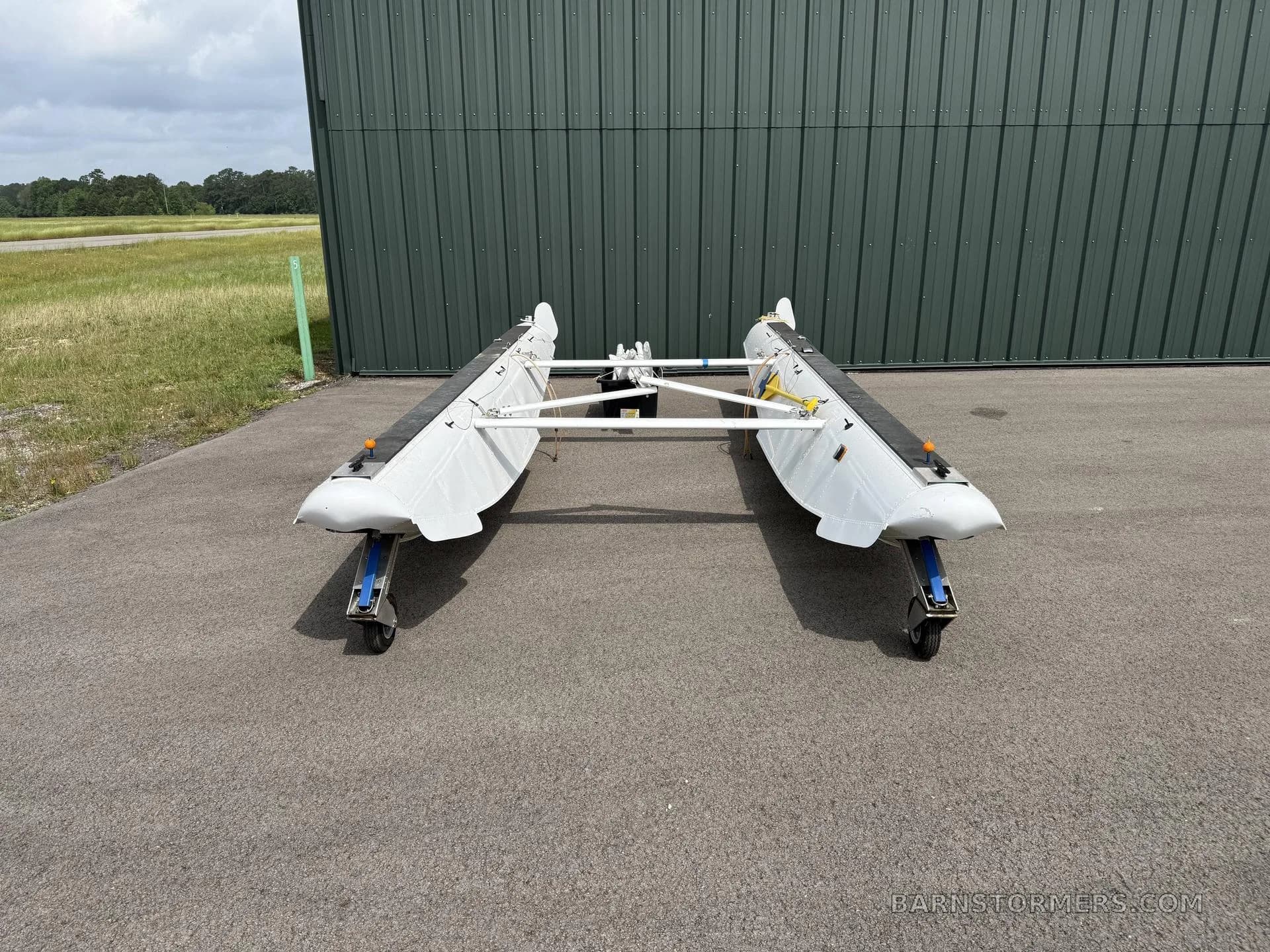 A front view of two white aircraft floats with wheels on an asphalt apron in front of a green hangar.