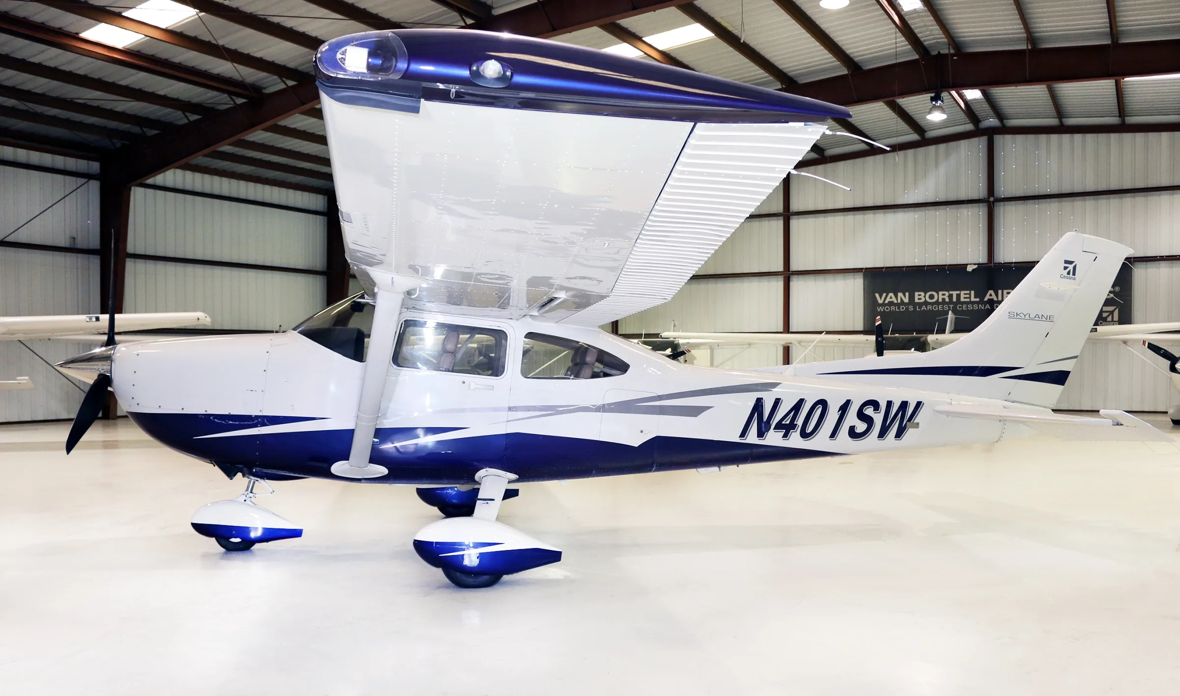 A side view of a white and blue Cessna Skylane aircraft with registration N401SW parked in a hangar.